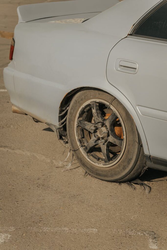 Close-up of a blue car with a severely damaged tire on weathered concrete.